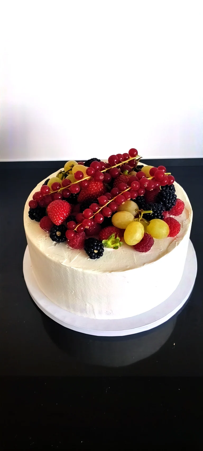 Gâteau blanc garni de fruits rouges et de raisins